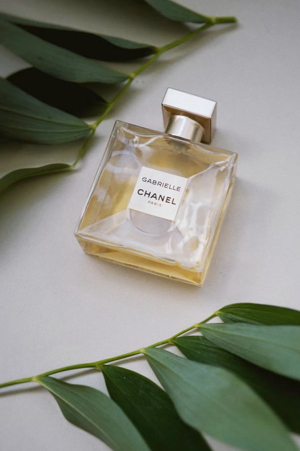 Perfume bottle named Gabrielle Essence Eau De Parfum placed on a table with two leaves in the background.